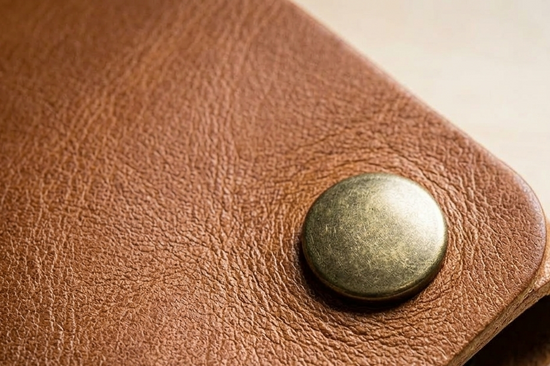 Close-up of a brown leather wallet with a metal button on a light background